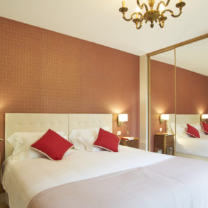 photo détail de la chambre Ausone, lit avec coussins rouge, tête de lit blanche et tapisserie ocre-rouge, chambres d'hôtes château Pont Saint-Martin, Pessac Léognan, Bordeaux, dégustation de vin, tout confort