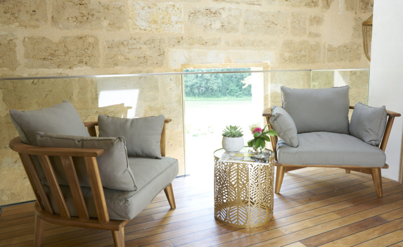 photo du palier, 2 fauteuils gris, table dorée ajourée et décorée, mur en pierre, château Pont Saint-Martin, chambres d'hôtes Pessac Léognan, Bordeaux, dégustation de vin